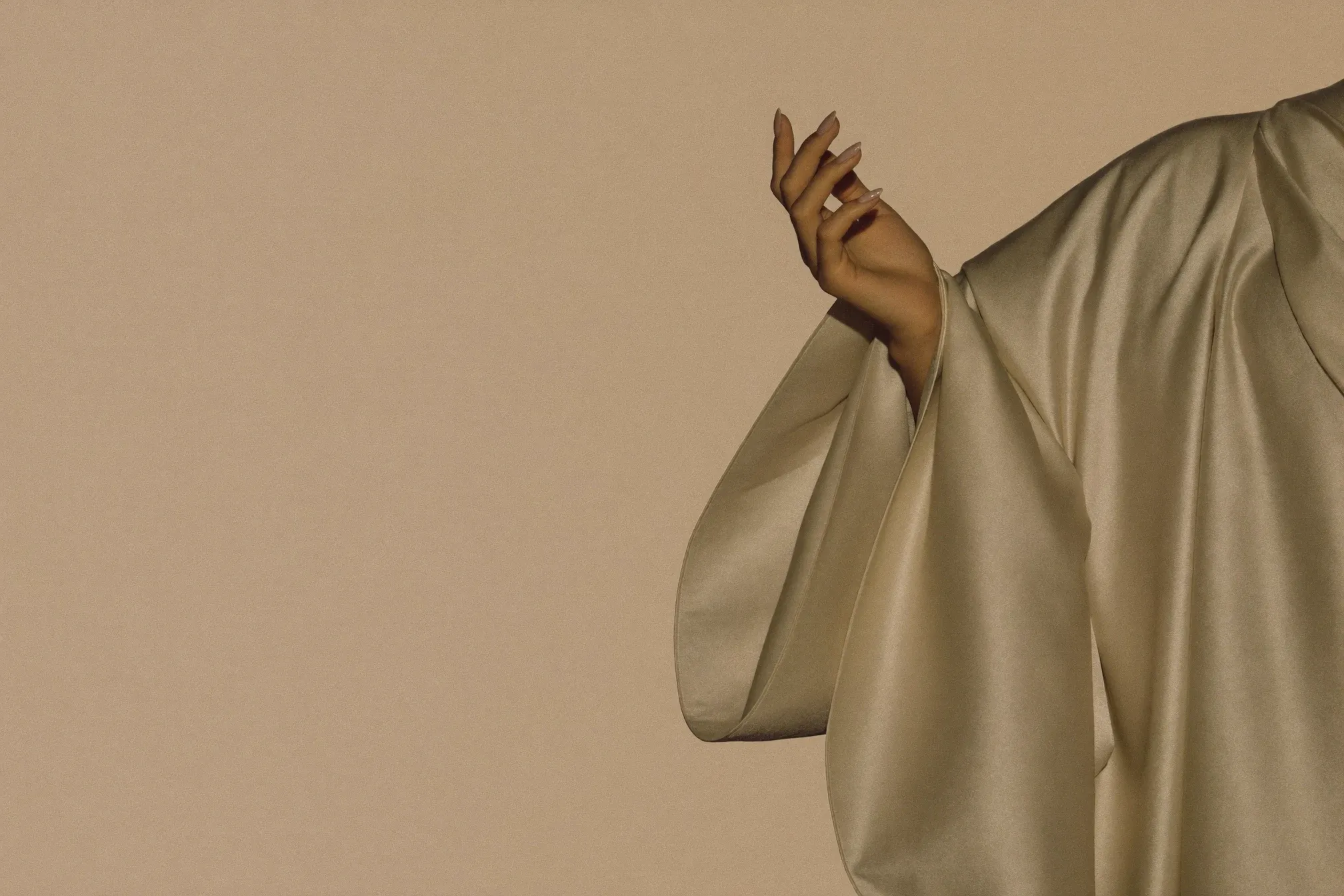 Hand with a sage manicure emerging from folds of bone-coloured silk