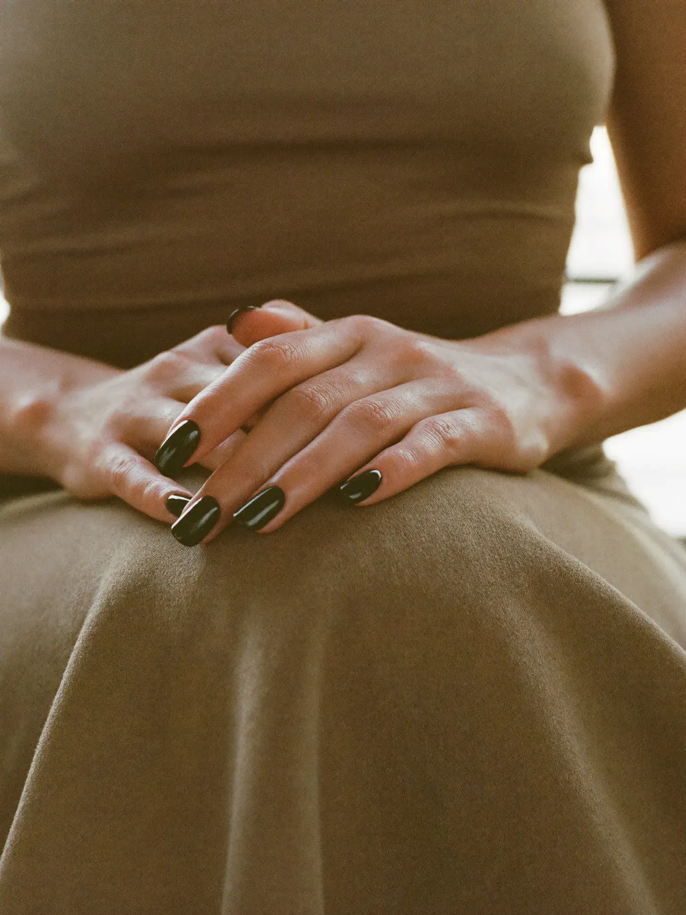 Hands with a glossy dark manicure resting on warm fabric
